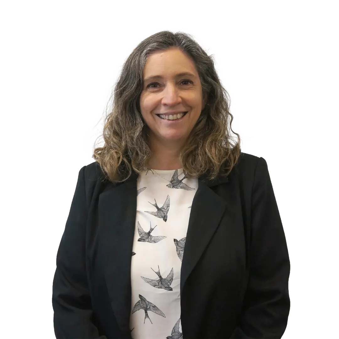 Retrato corporativo de Alicia Moraga sonriendo, con blazer negro y blusa blanca con estampado de pájaros sobre fondo blanco, en una pose profesional.