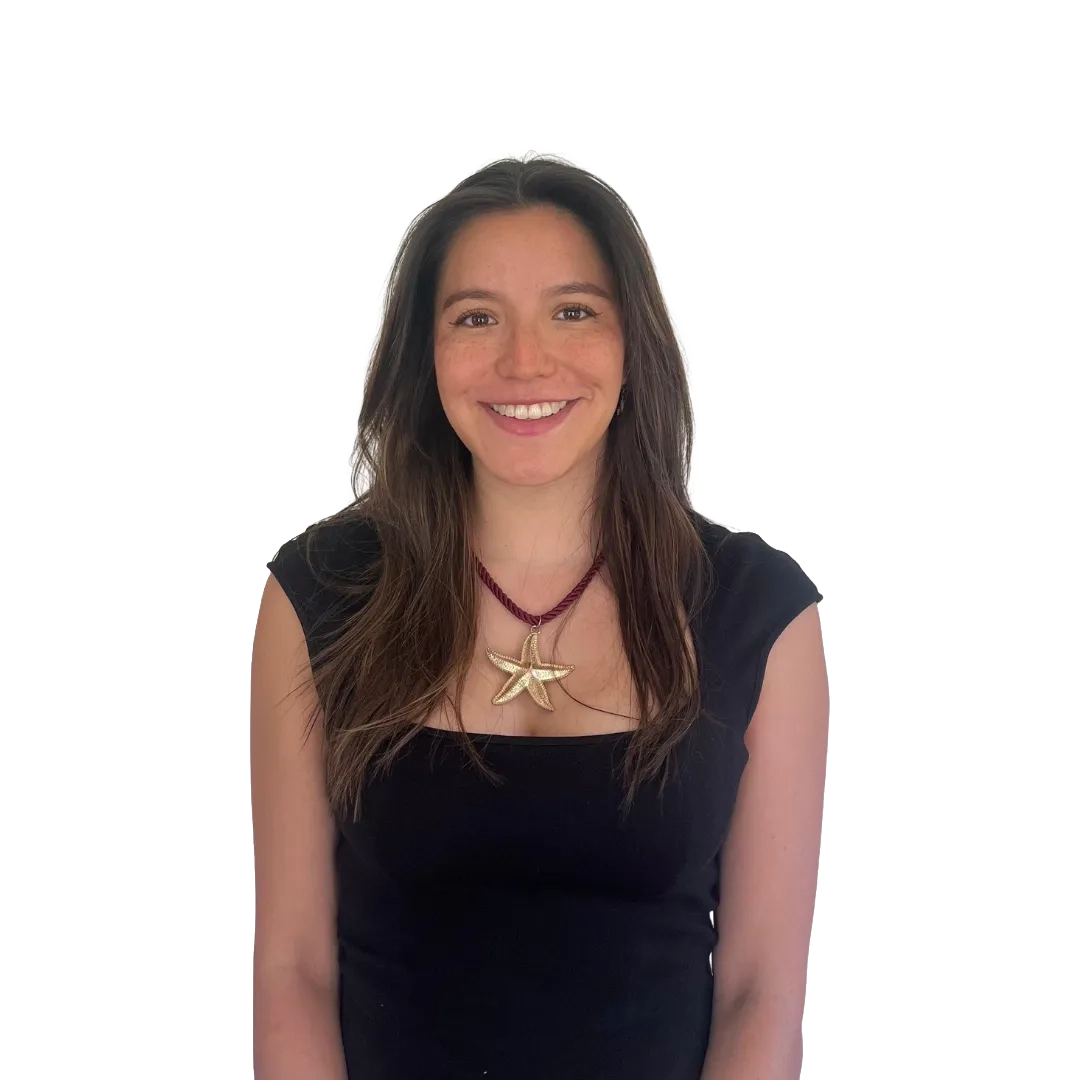 Retrato corporativo de Antonia Nicholls sonriendo, con polera negra sin mangas y collar con colgante de estrella de mar sobre fondo blanco, en una pose profesional.