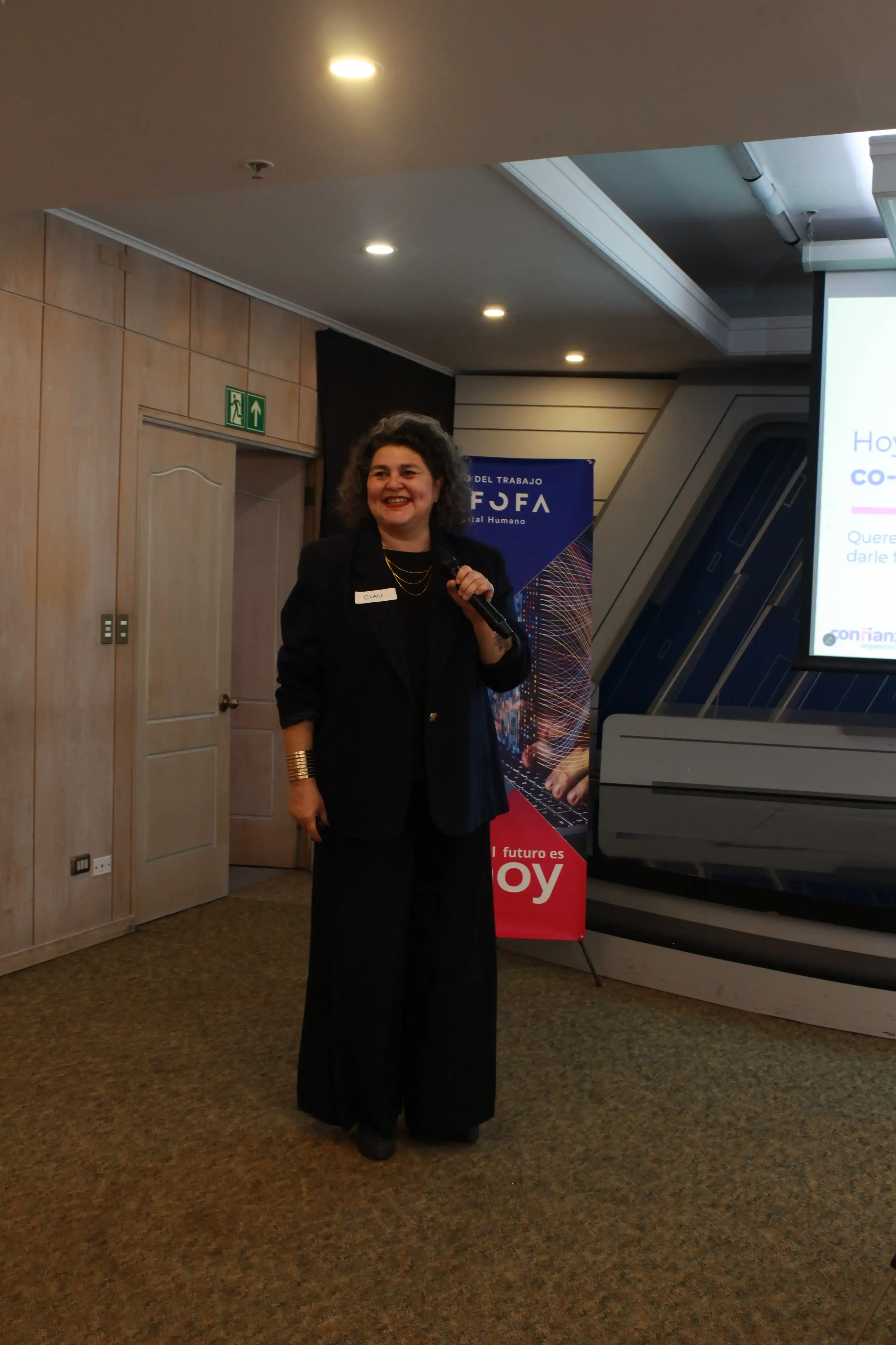 Claudia Picero presenta una exposición con micrófono frente a los asistentes durante el Primer Encuentro de la Comunidad de Empresas por la Confianza.