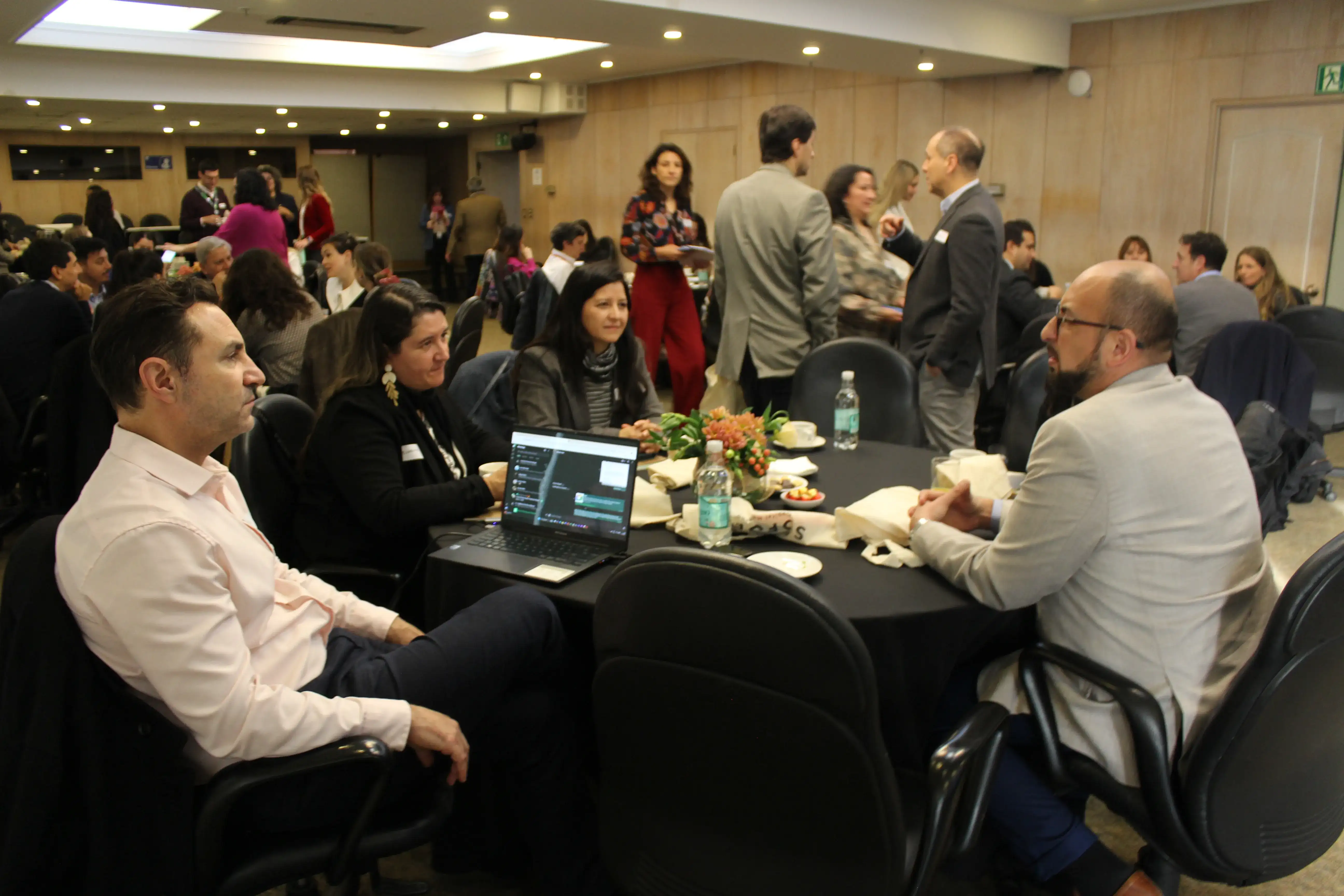 Participantes conversan en distintas mesas mientras comparten ideas y materiales durante una actividad colaborativa.