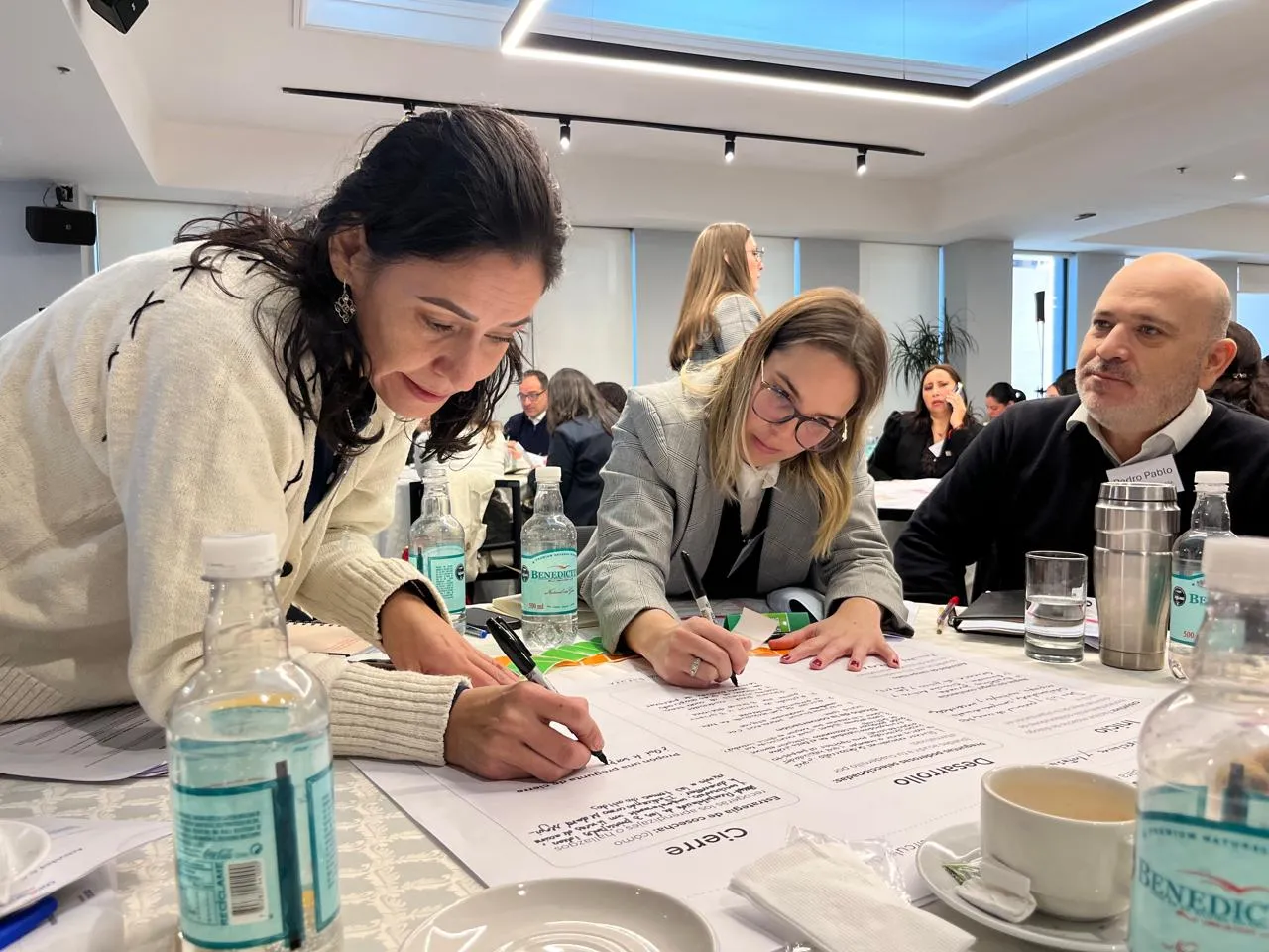 Participantes completan una guía de conversación mientras una facilitadora acompaña el trabajo realizado en la mesa.